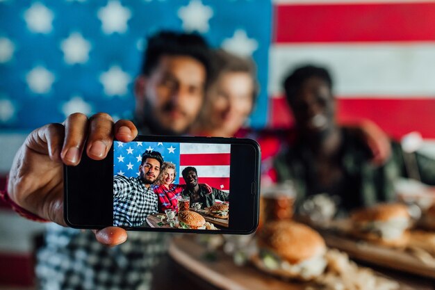 Giovani amici in un fast food che si fanno selfie mentre mangiano hamburger e bevono birra