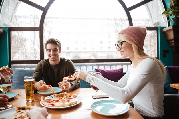 Giovani amici nel caffè mangiando pizza bevendo alcolici.