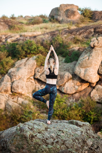 Giovani asana allegri di yoga di addestramento della donna su roccia in canyon