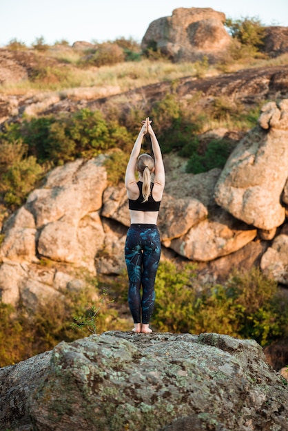 Giovani asana allegri di yoga di addestramento della donna su roccia in canyon