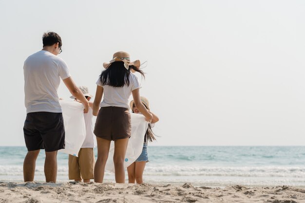 Giovani attivisti felici asiatici della famiglia che raccolgono rifiuti di plastica e che camminano sulla spiaggia. I volontari asiatici aiutano a mantenere la natura a ripulire la spazzatura. Concetto sui problemi di inquinamento ambientale.