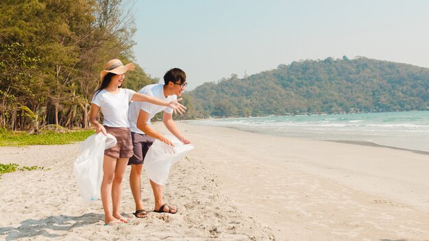 Giovani attivisti felici asiatici della famiglia che raccolgono rifiuti di plastica sulla spiaggia. I volontari asiatici aiutano a mantenere la natura pulita e a raccogliere i rifiuti. Concetto sui problemi di inquinamento ambientale.