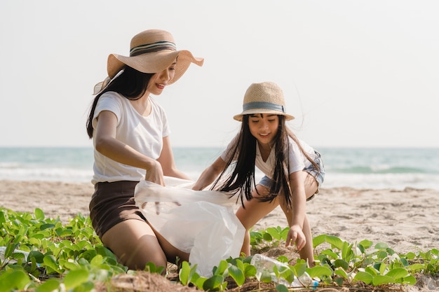 Giovani attivisti felici asiatici della famiglia che raccolgono rifiuti di plastica sulla spiaggia. I volontari asiatici aiutano a mantenere la natura pulita e a raccogliere i rifiuti. Concetto sui problemi di inquinamento ambientale.