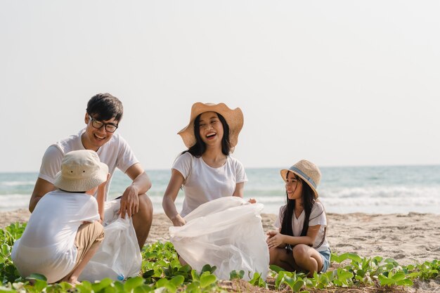 Giovani attivisti felici asiatici della famiglia che raccolgono rifiuti di plastica sulla spiaggia. I volontari asiatici aiutano a mantenere la natura pulita e a raccogliere i rifiuti. Concetto sui problemi di inquinamento ambientale.