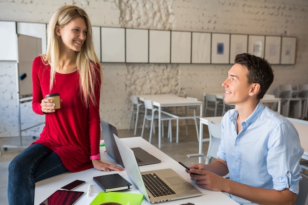 Giovani attraenti che lavorano insieme in linea nella stanza dell'ufficio co-working open space