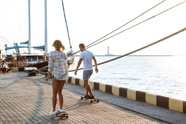 Giovani belle coppie che camminano in riva al mare, skateboard.