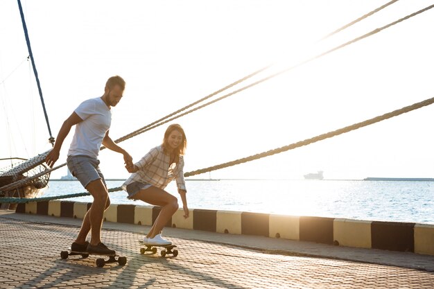 Giovani belle coppie che camminano in riva al mare, skateboard.