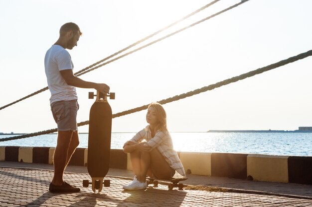 Giovani belle coppie che camminano in riva al mare, skateboard.