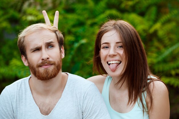 Giovani belle coppie che posano, sorridenti, mostrando la lingua, camminando nel parco