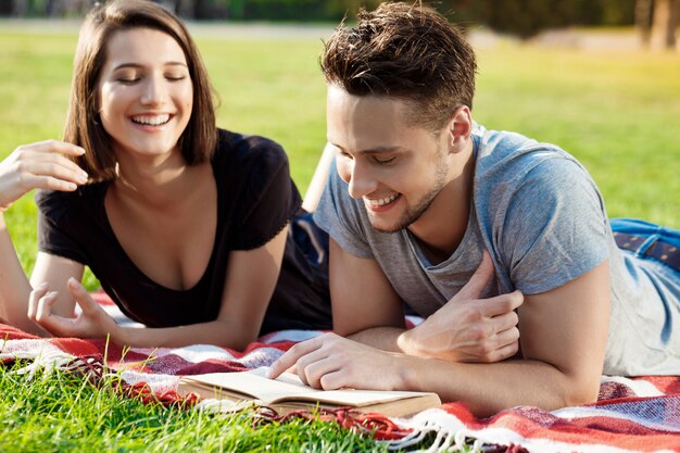 Giovani belle coppie che sorridono, che leggono, riposanti al parco