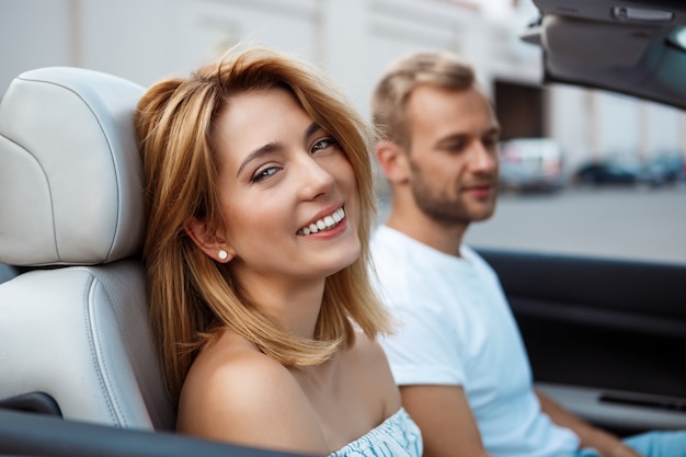 Giovani belle coppie che sorridono, sedendosi in automobile vicino al litorale.