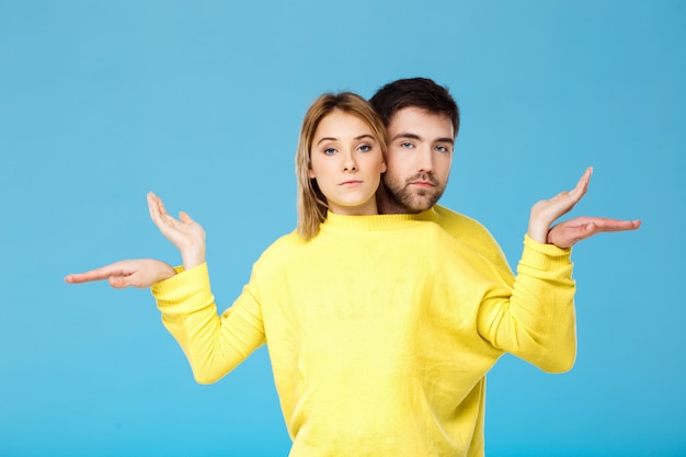 Giovani belle coppie in un maglione giallo che posa sorridere divertendosi sopra la parete blu