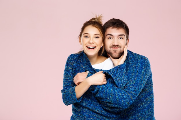 Giovani belle coppie in un maglione tricottato blu che posa sorridere divertendosi sopra la parete rosa-chiaro