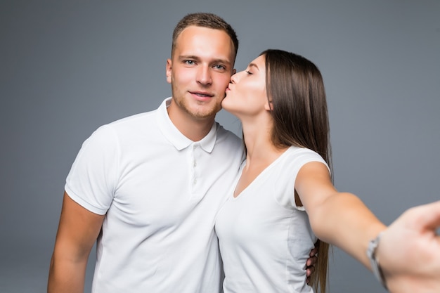 Giovani belle coppie nell'amore che prendono la foto romantica del selfie dell'autoritratto insieme al telefono cellulare che sorride felice che indossa vestiti alla moda isolati su fondo grigio