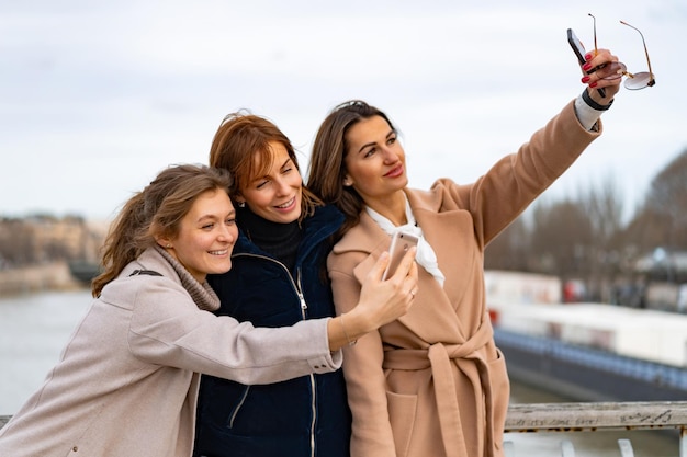 giovani belle donne amiche viaggiano, si fanno selfie sullo smartphone, ridono. Parigi. Il concetto di una foto di viaggio felice. Giovani felici che si fanno selfie in città