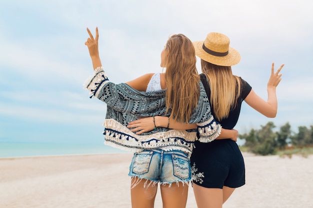 Giovani belle donne hipster in vacanza sulla spiaggia tropicale, vestito estivo elegante, felice, tendenza della moda, stile hippie, accessori alla moda, amiche insieme, stato d'animo positivo, vista dal retro