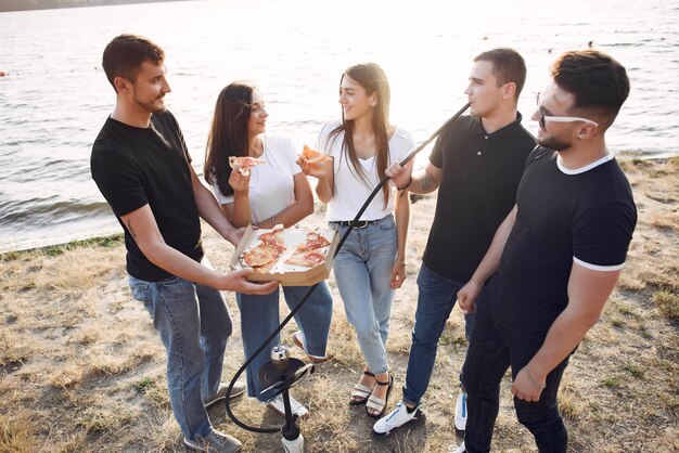 Giovani che mangiano pizza e che fumano shisha sulla spiaggia