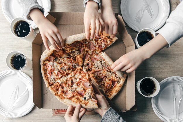 Giovani che prendono fette di pizza calda da una scatola di cartone a vista dall'alto del tavolo