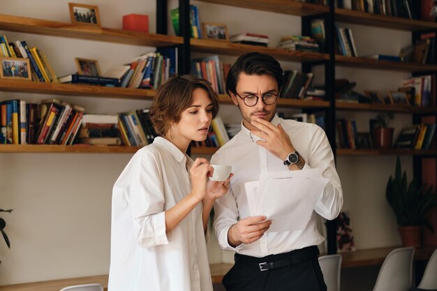 Giovani colleghi di lavoro pensierosi in piedi con documenti che discutono premurosamente di lavorare insieme in un ufficio moderno