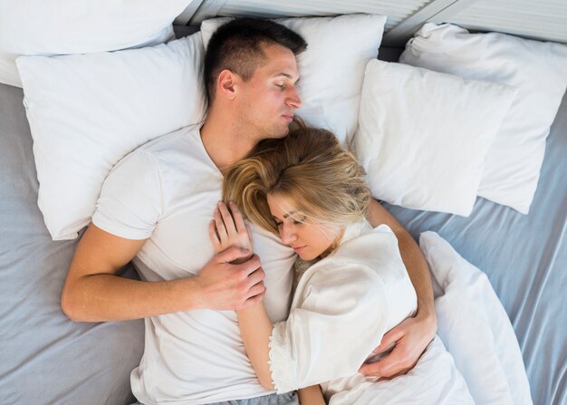 Giovani coppie addormentate che abbracciano sul letto