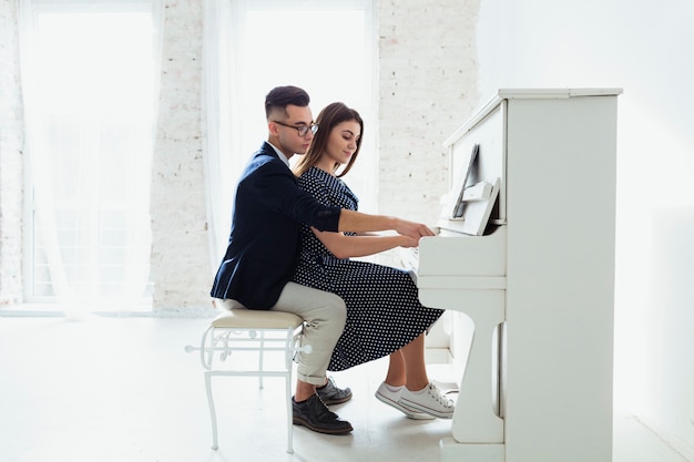 Giovani coppie adorabili che giocano insieme il piano a casa