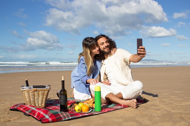 Giovani coppie adorabili che prendono selfie in riva al mare