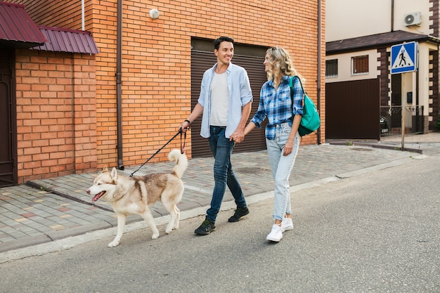 Giovani coppie alla moda che camminano con il cane in strada. uomo e donna felici insieme alla razza husky,