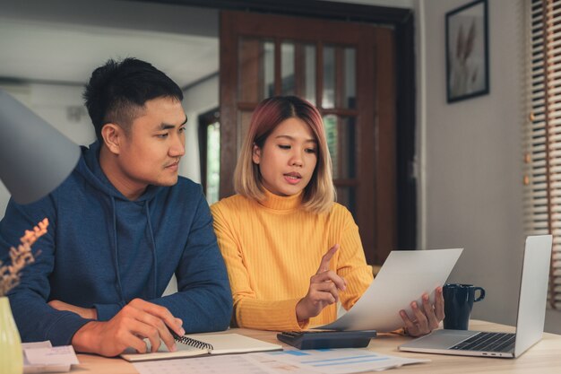 Giovani coppie asiatiche che gestiscono le finanze, esaminando i loro conti bancari facendo uso del computer portatile