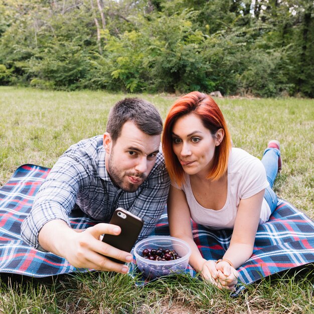 Giovani coppie che catturano selfie sul cellulare al picnic all&#39;aperto