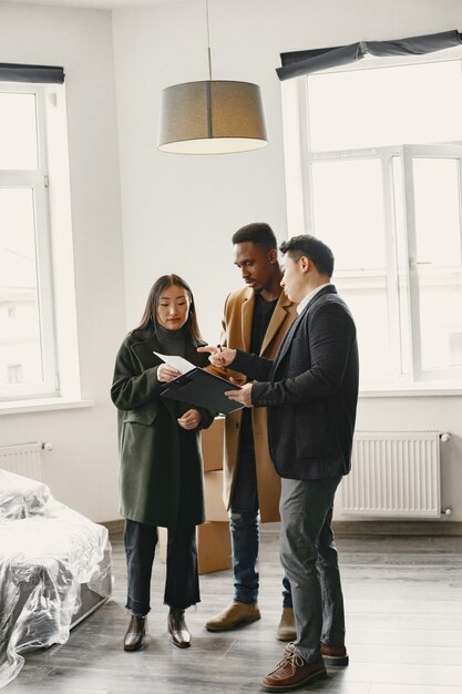 Giovani coppie che comprano una nuova casa. Donna asiatica e uomo africano. Firma dei documenti nella nuova casa.