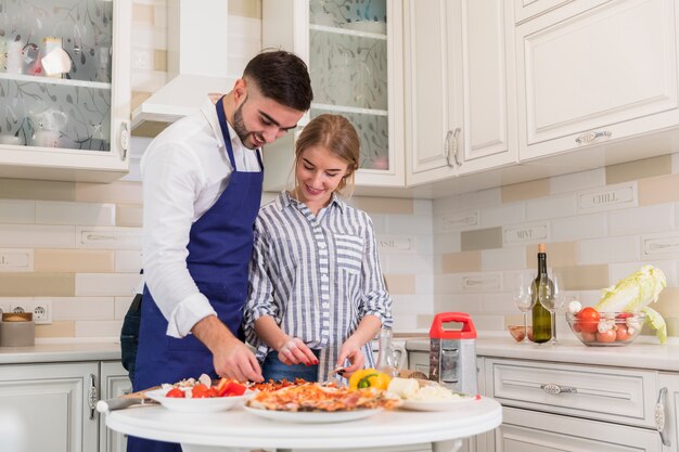 Giovani coppie che cucinano pizza in cucina