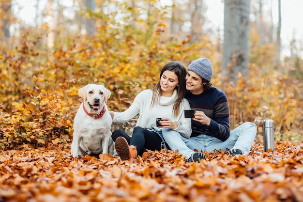 Giovani coppie che fanno picnic con il loro labrador dorato nel parco, sdraiato su una coperta.