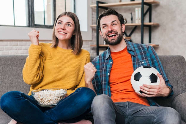 Giovani coppie che guardano il gioco di calcio che incoraggia dopo la conquista