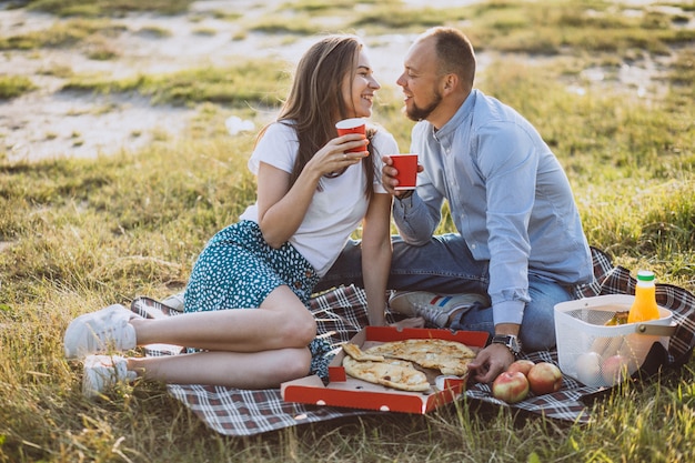 Giovani coppie che hanno picnic con pizza in parco