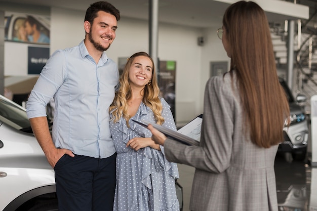 Giovani coppie che parlano con il commerciante di automobile femminile