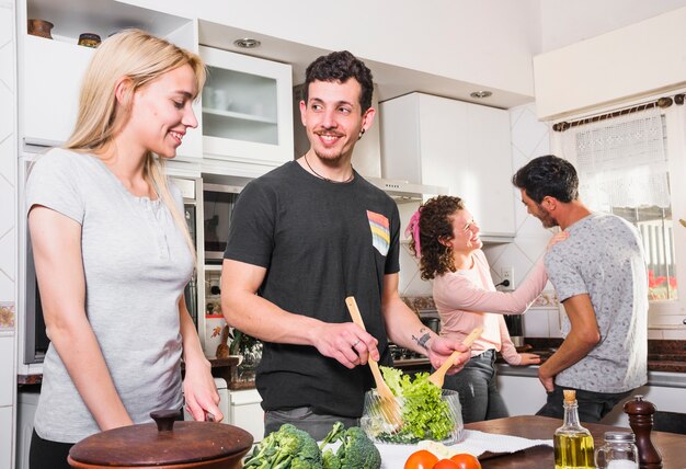 Giovani coppie che preparano insalata e i loro amici a parlare a vicenda a sfondo in cucina