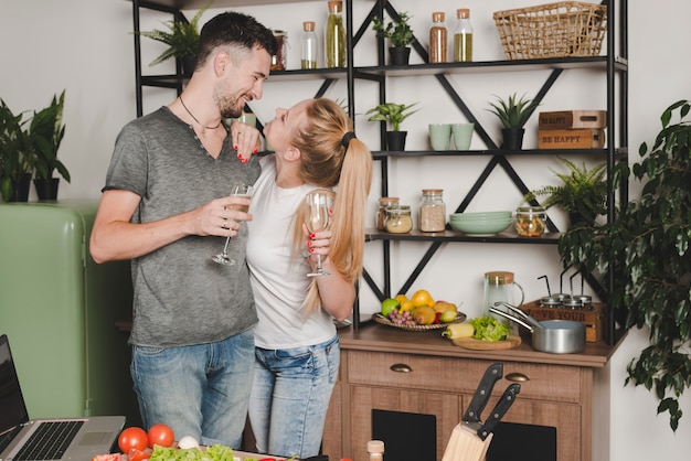 Giovani coppie che se lo esaminano che tiene flute di champagne nella cucina