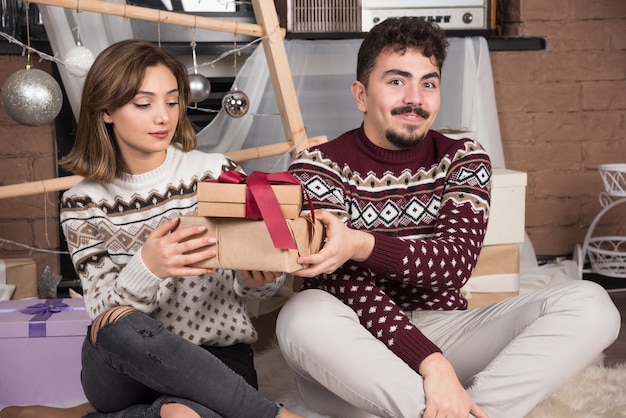 Giovani coppie che si siedono con i regali di Natale vicino alle palle d'argento festive.