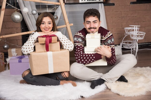 Giovani coppie che si siedono con i regali di Natale vicino alle palle d'argento festive.