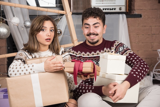 Giovani coppie che si siedono con i regali di Natale vicino alle palle d'argento festive.