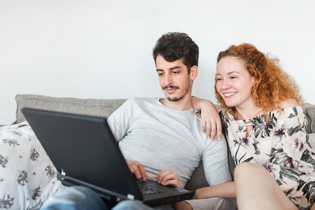 Giovani coppie che si siedono sul sofà facendo uso del computer portatile