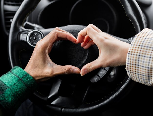 Giovani coppie che viaggiano con auto da vicino facendo a forma di cuore