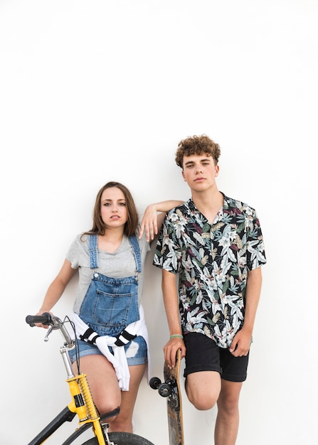 Giovani coppie con la bicicletta e il pattino che si levano in piedi sulla priorità bassa bianca