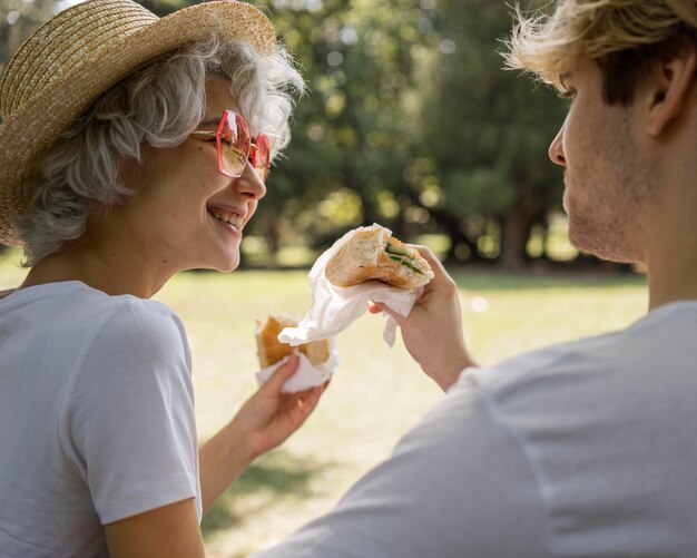 Giovani coppie di smiley che mangiano hamburger insieme nel parco