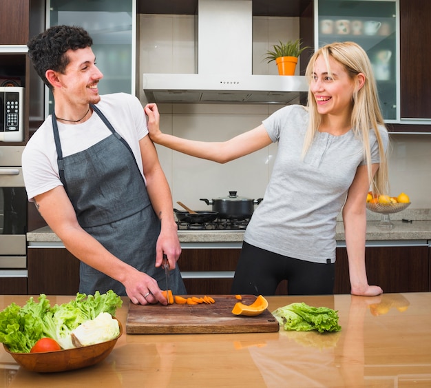 Giovani coppie divertendosi mentre tagliando le verdure in cucina