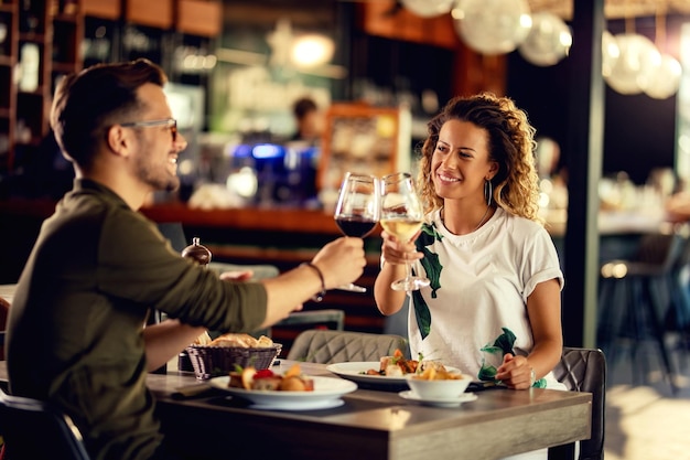 Giovani coppie felici che celebrano e brindano con i bicchieri da vino mentre mangiano in un ristorante
