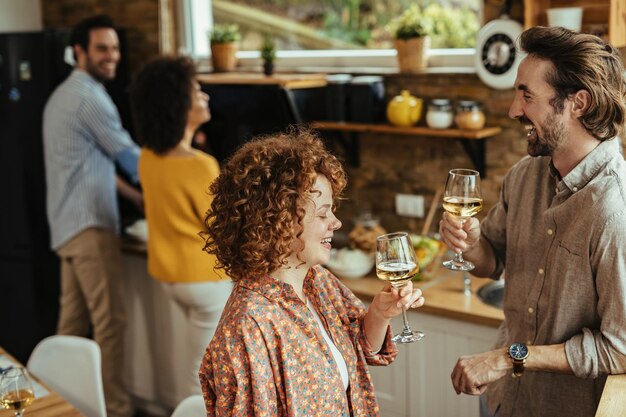 Giovani coppie felici che comunicano e bevono vino mentre i loro amici preparano il cibo in background