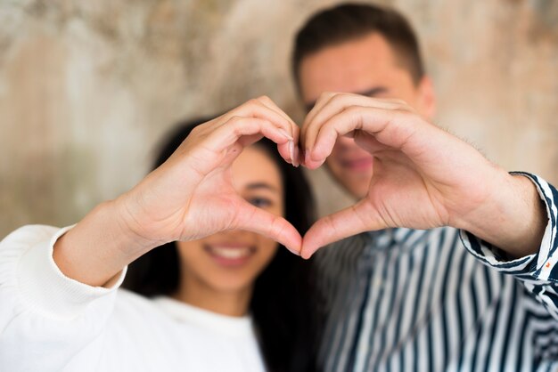 Giovani coppie felici che gesturing cuore con le mani