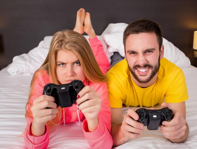 Giovani coppie felici che si divertono a giocare ai videogiochi a letto.