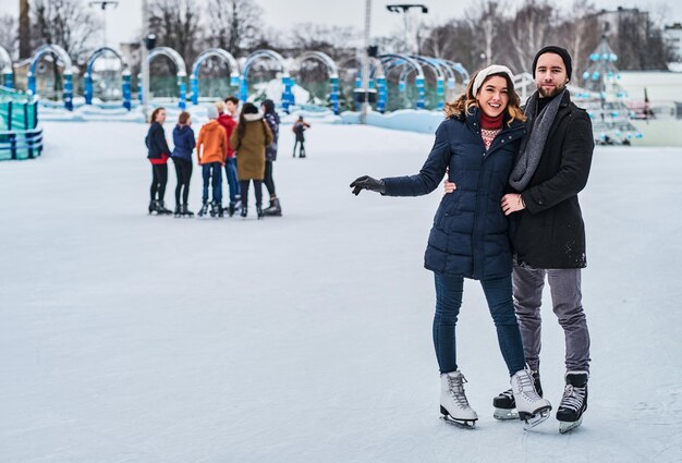 Giovani coppie felici che si incontrano sulla pista di pattinaggio, si abbracciano e si godono l'orario invernale